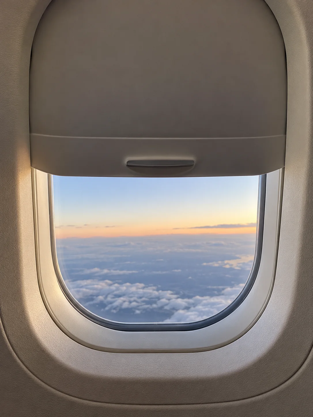 Oblò dell’aereo con tendina parzialmente abbassata e luce del mattino